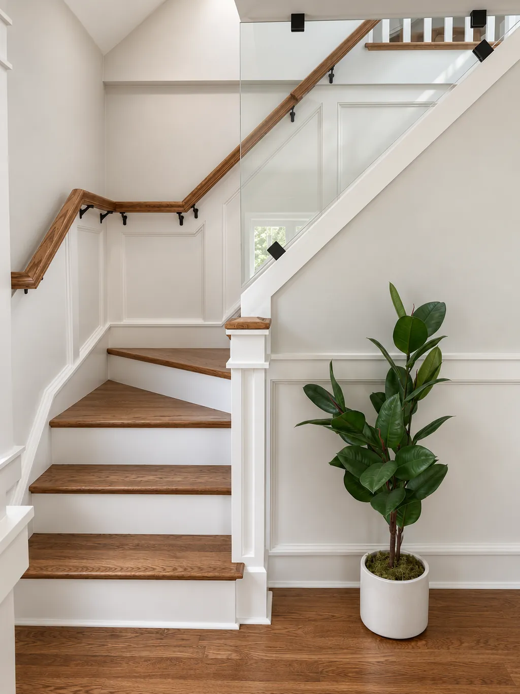 Winder staircase with oak treads, a continuous oak wall rail and a glass guard, framed by wall panel millwork